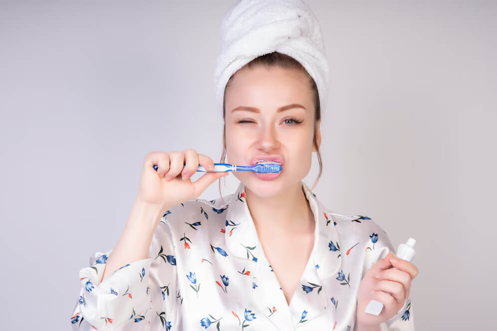 a woman brushing her teeth while holding a tooth paste