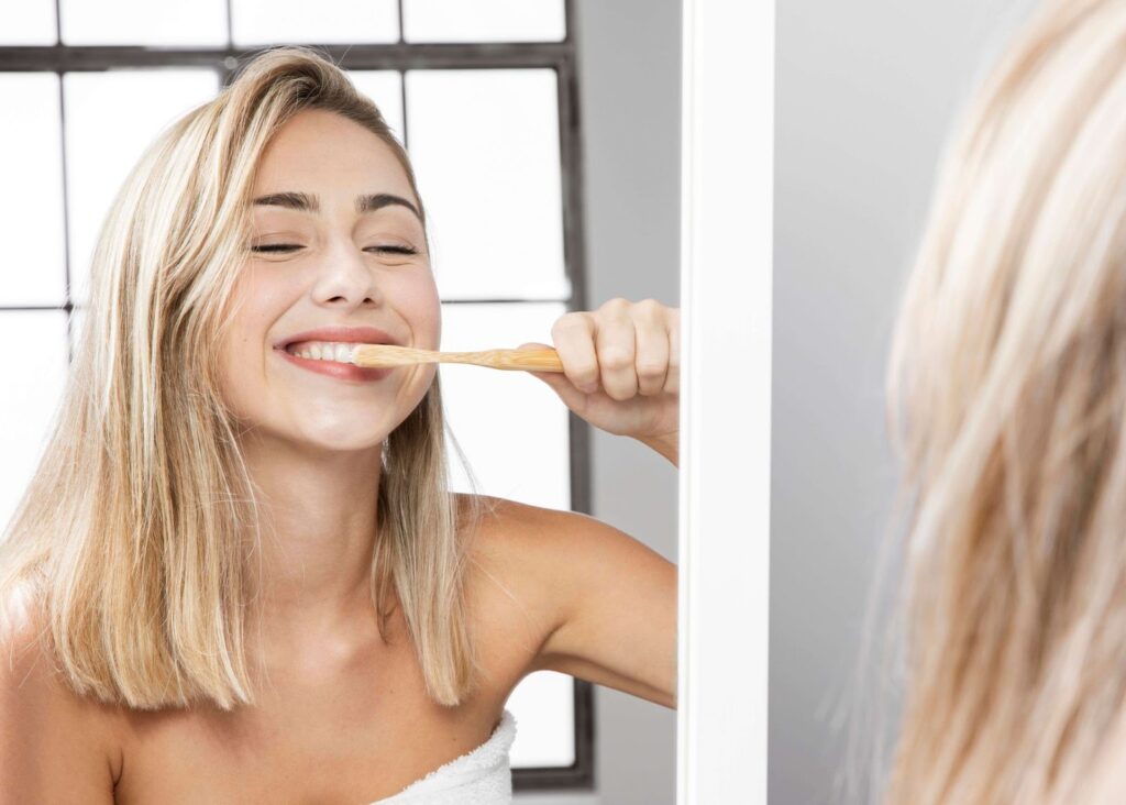 a woman happily brushing her teeth in front of a wide mirror